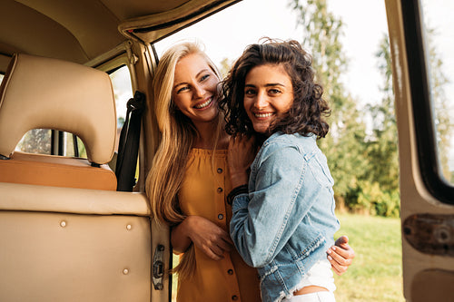 Young smiling women embracing while standing at camper van