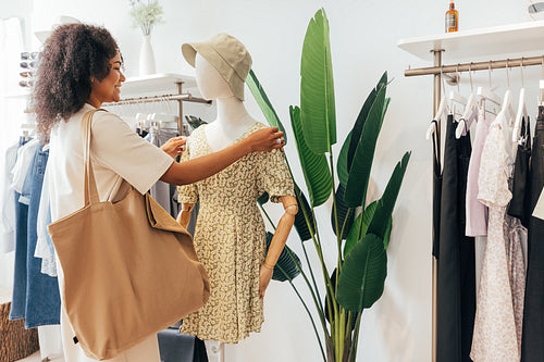 Stylish woman with big shopper bag standing at a mannequin in a boutique while looking new clothes