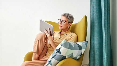 Stylish senior woman holding a digital tablet while sitting in living room