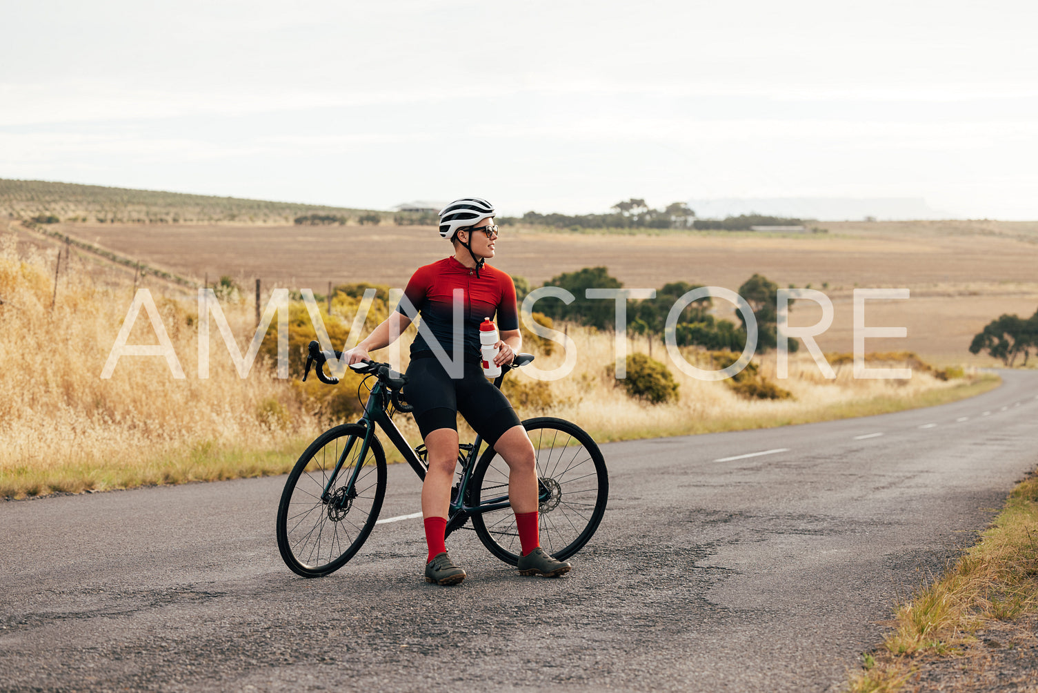 Professional female cyclist taking a break from cycling and holding a bottle of water on empty road