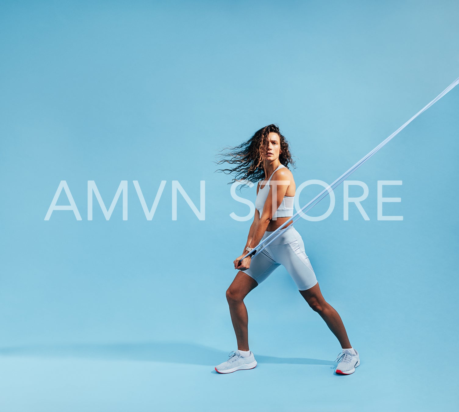 Female athlete doing intense stretching exercises with elastic band. Healthy woman in sportswear working out on blue background.