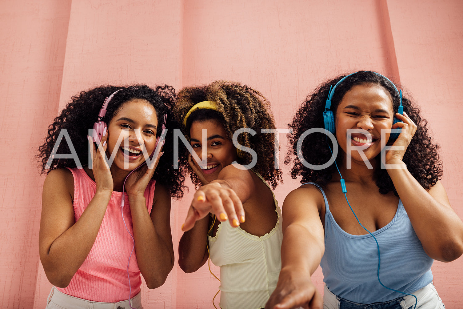 Three laughing women with curly hair dancing together and looking at camera, wearing headphones