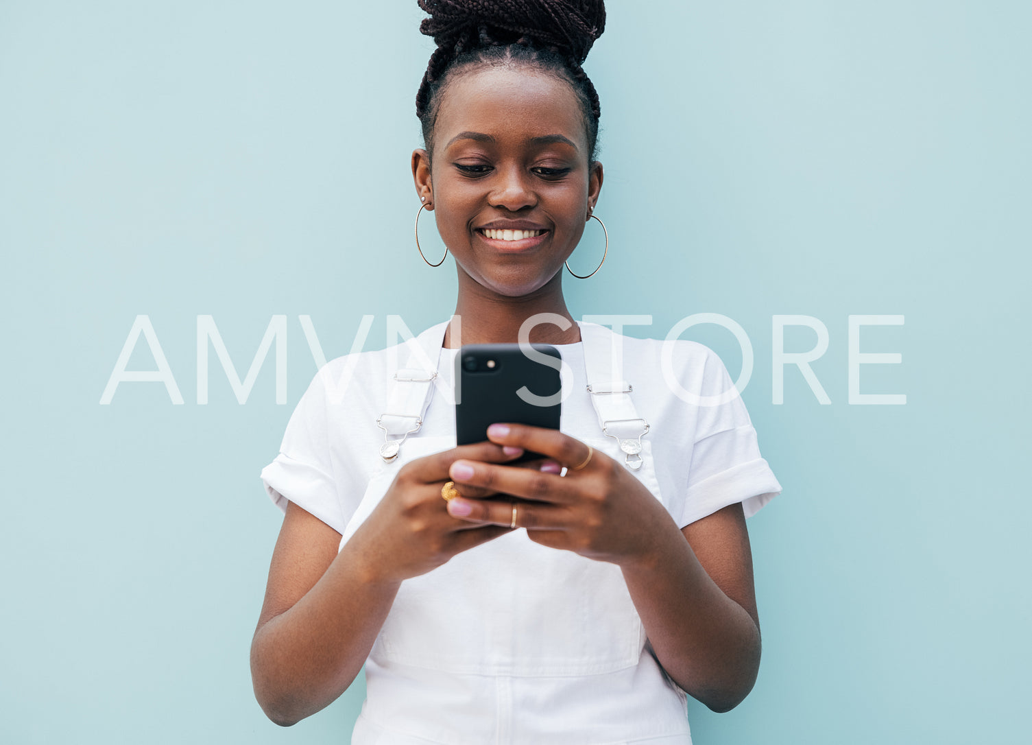 Smiling woman in white casual clothes typing on a smartphone while standing outdoors at blue wall