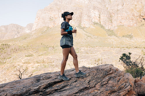 Side view of young female hiker standing with bottle water. Woman taking break after hike on mountain path.