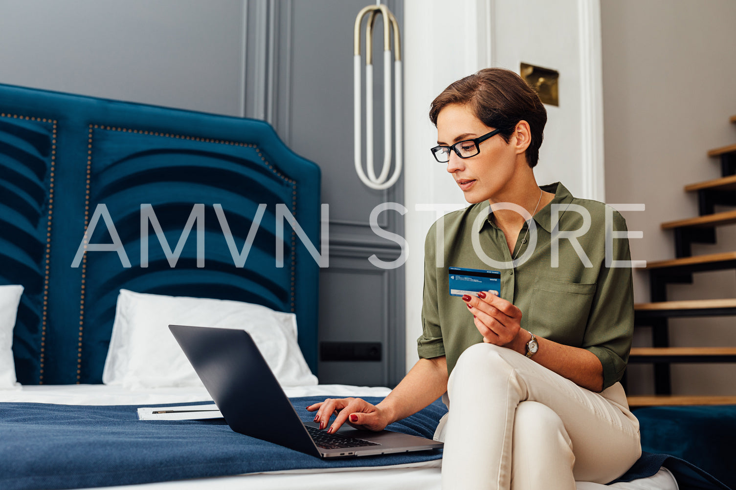 Woman sitting on hotel room bed with laptop and credit card. Businesswoman typing on keyboard and making online order.	