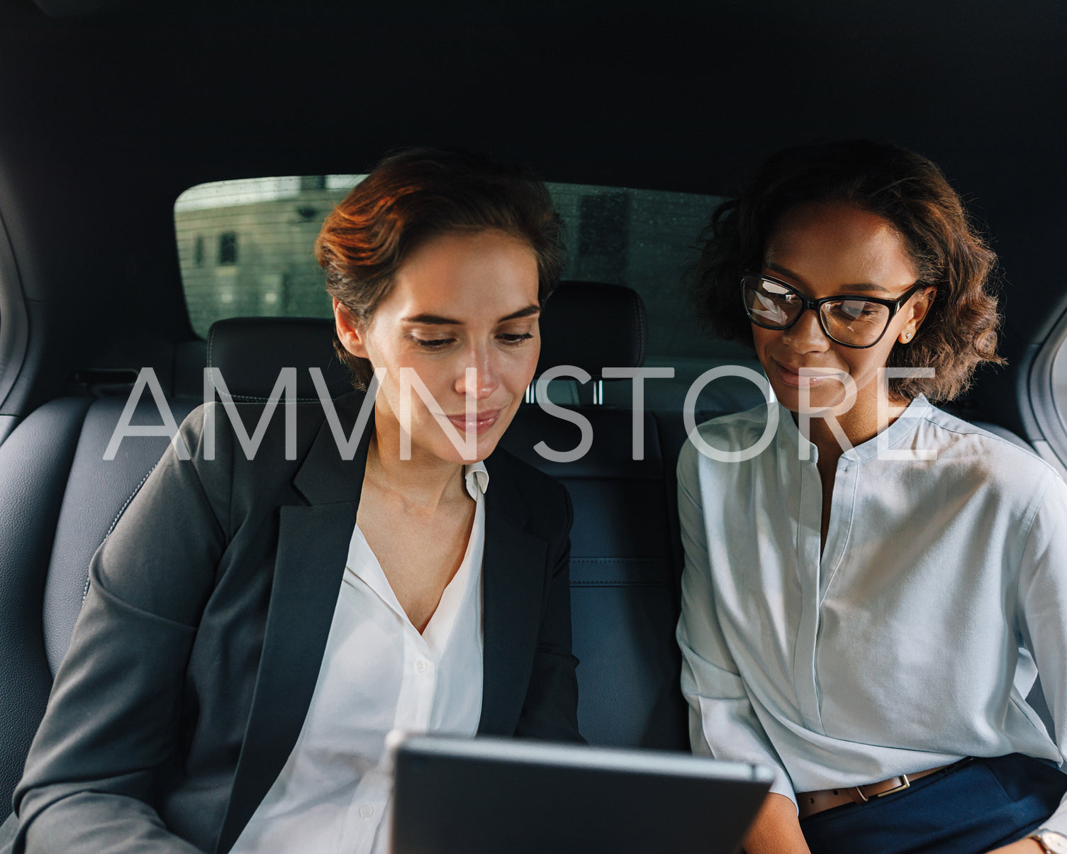 Two business people using digital tablet in taxi	