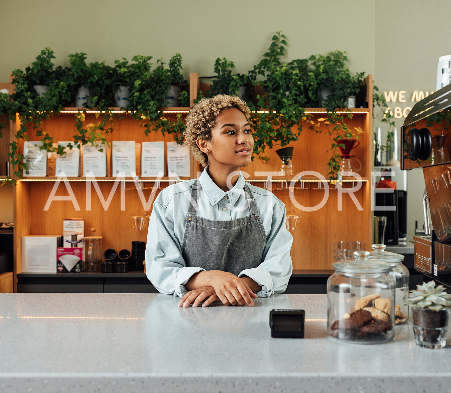 Young woman in an apron standing in a coffee shop. Female with short hair standing at her cafe.