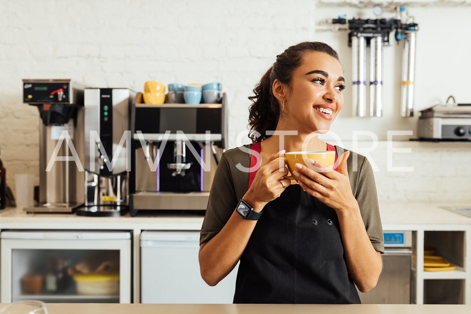 Female waitress holding coffee mug while standing at table in coffee shop	