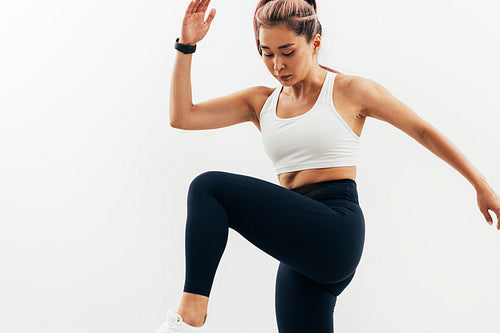 Young Asian woman doing warming up exercises against white wall