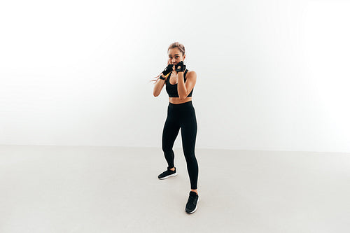 Shot of a female boxer holding a stance. Woman in gloves exercising indoors.