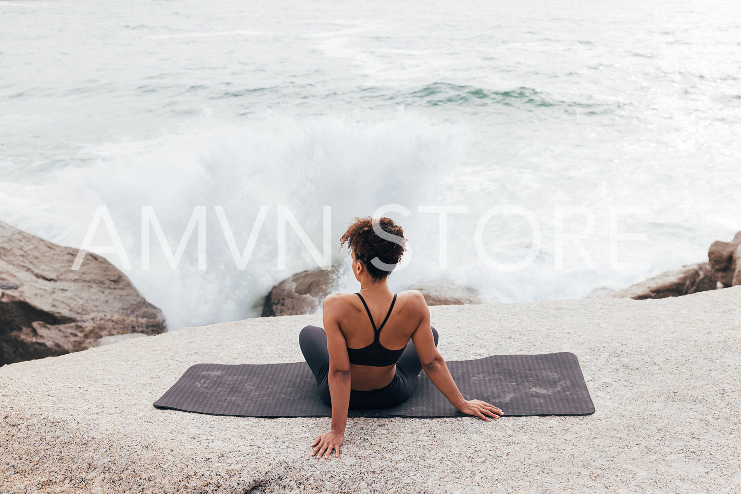 Back view of female in fitness wear looking on waves while sitting on a yoga mat