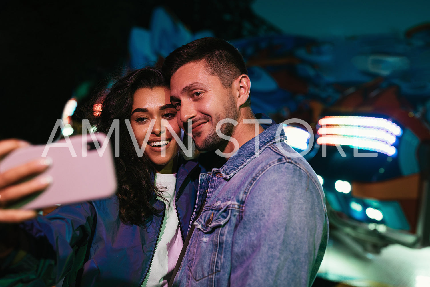 Young smiling people taking selfie at night in an amusement park