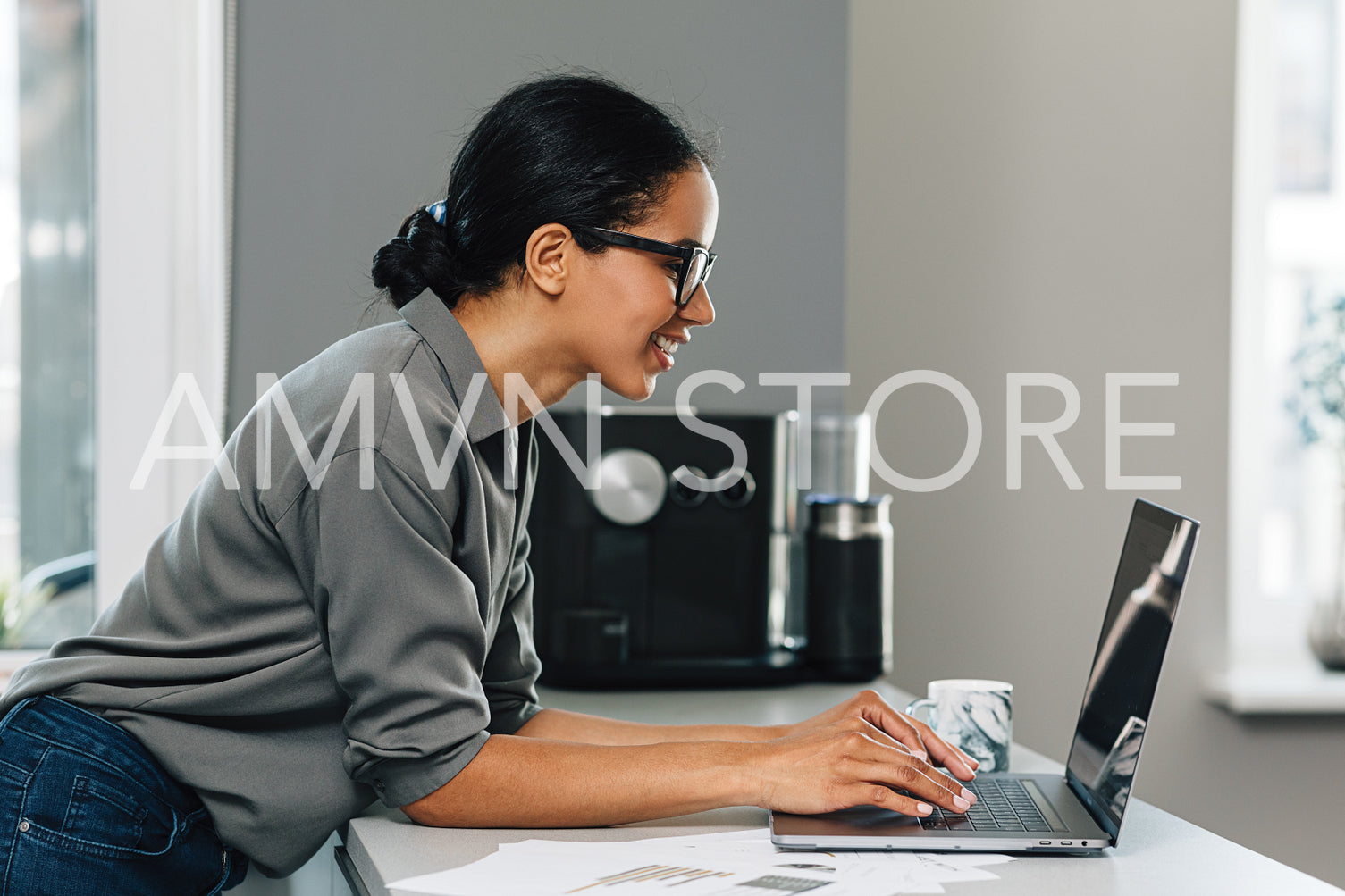 Side view of a young woman working from her kitchen, typing on laptop	