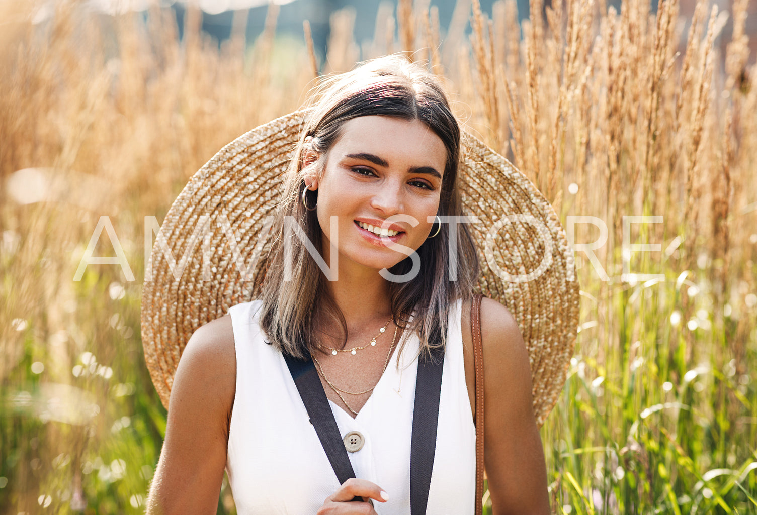 Beautiful young woman standing on the field with straw hat and looking at camera	