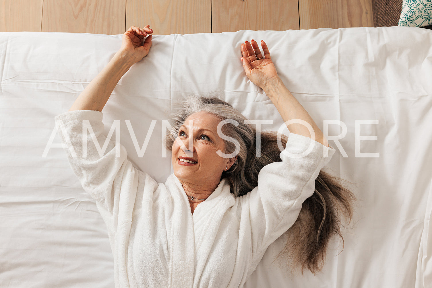 Pleased senior woman lying on a bed wearing bathrobe