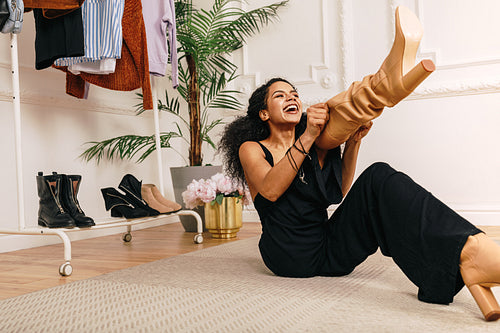 Happy woman pull on knee-high boot on a leg while sitting on a floor