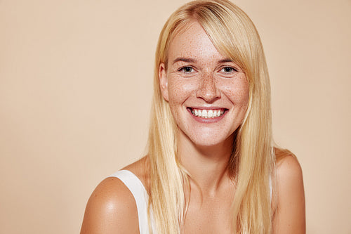 Cheerful blond female with perfect smooth skin looking at camera. Portrait of a happy freckled woman looking straight at a camera.