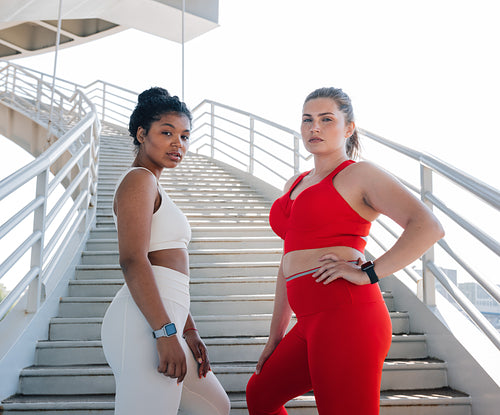 Two women in sportswear with different colors posing together while standing on a staircase outdoors.