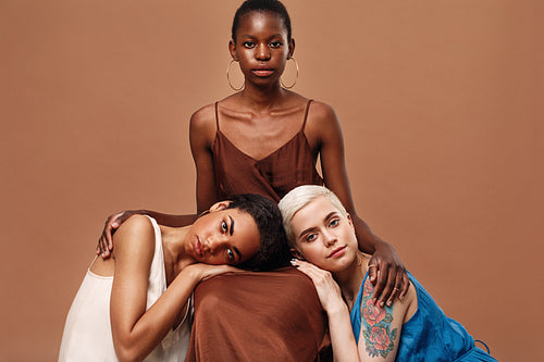 Three beautiful women posing together in a studio wearing dresses