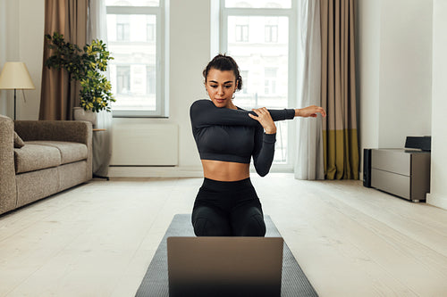 Young woman repeating exercises while watching online exercise session on her laptop in the living room