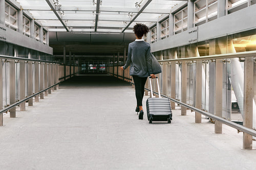 Businesswoman walking with suitcase in corridor, back view