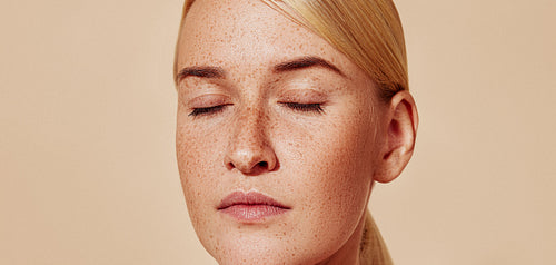 Close-up studio shot of a young beautiful blond woman with freckles. Cropped shot of female with smooth skin.
