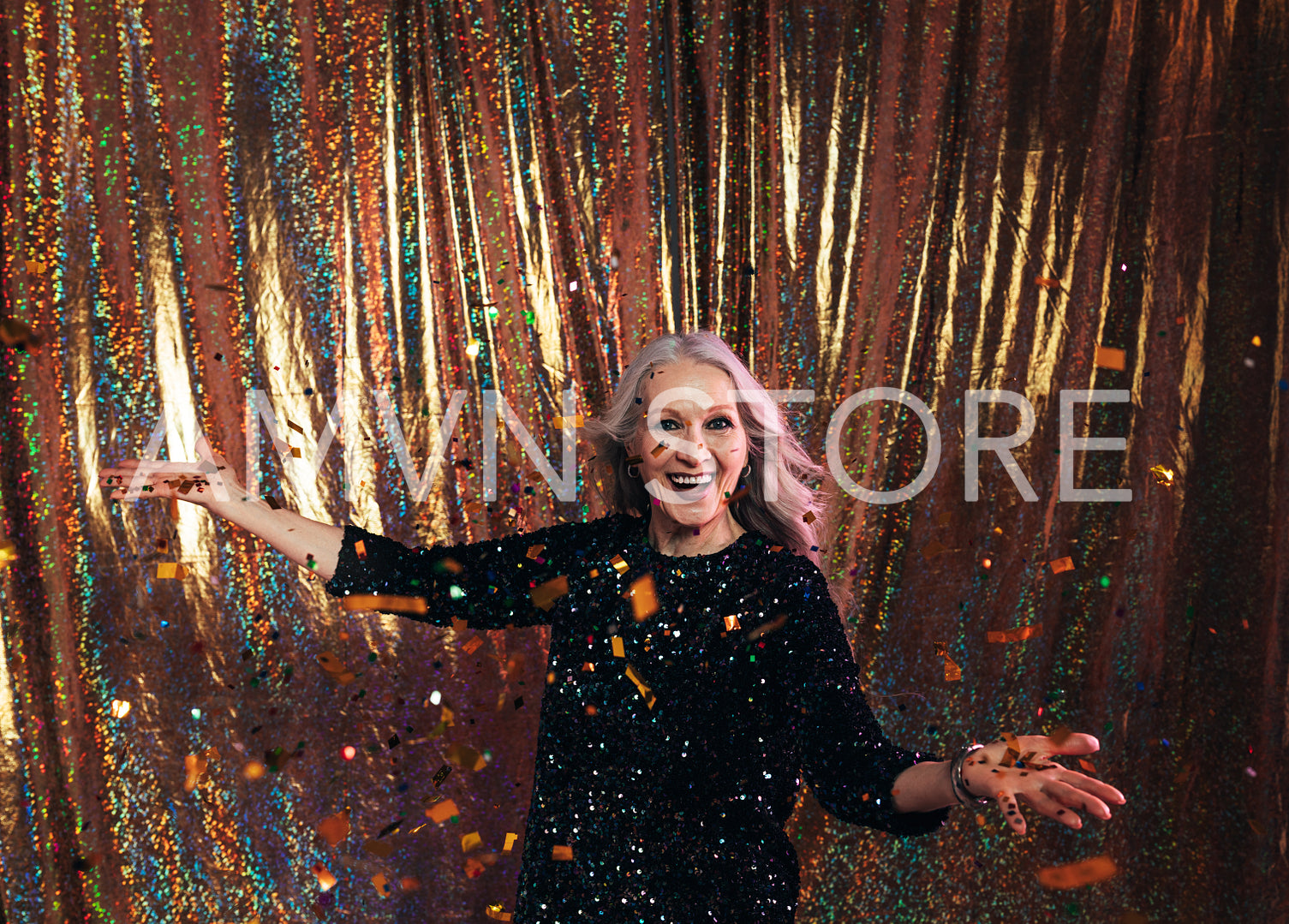 Happy senior woman in black dress standing under confetti agains