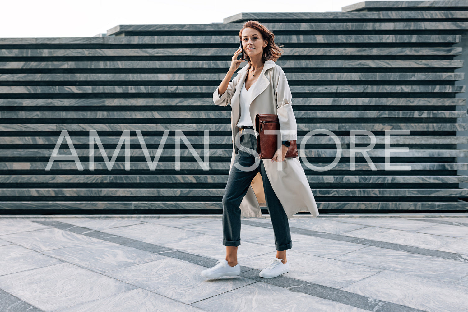 Full length of a walking middle-aged businesswoman with a folder talking on a mobile phone