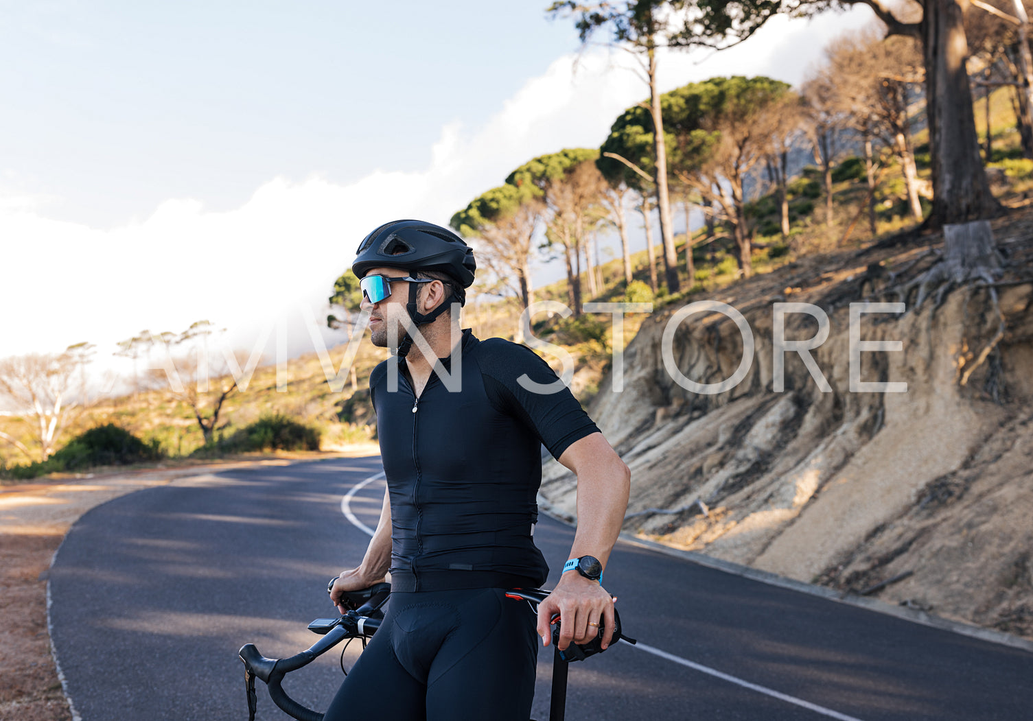 Side view of a professional biker relaxing leaning on his road bike. Male cyclist in glasses and helmet enjoying the view and taking a break during the ride.