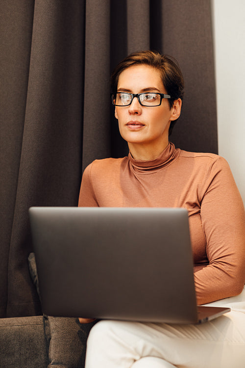 Young woman sitting on sofa in hotel room using laptop