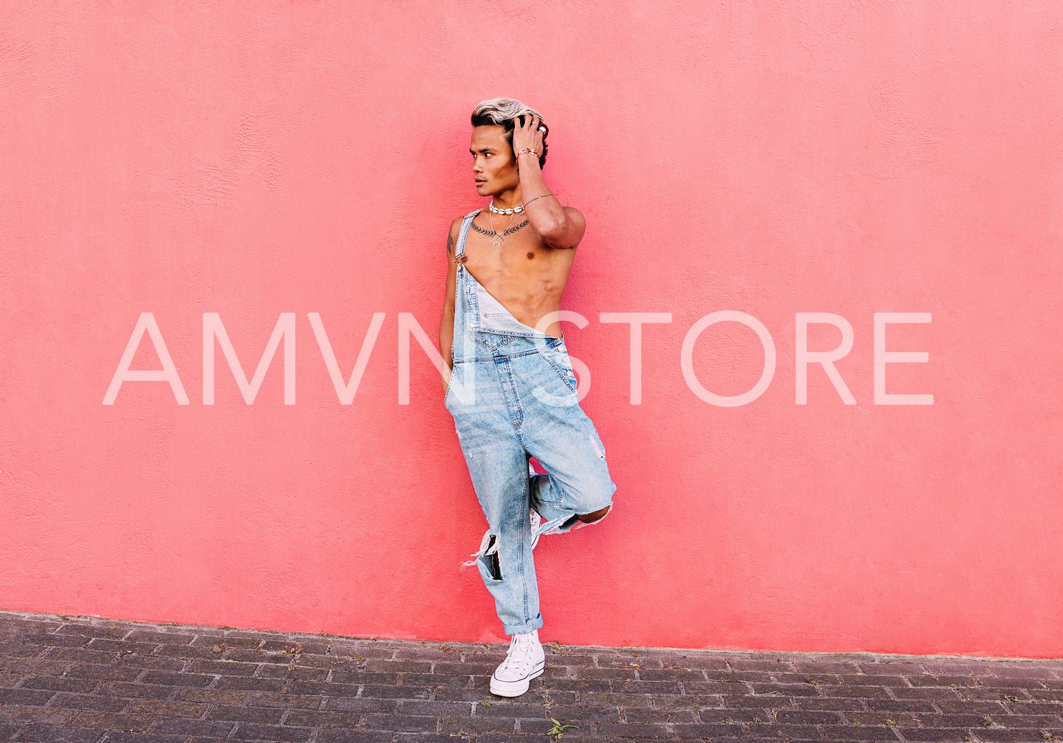 Stylish guy in casuals standing on one leg leaning on pink wall 