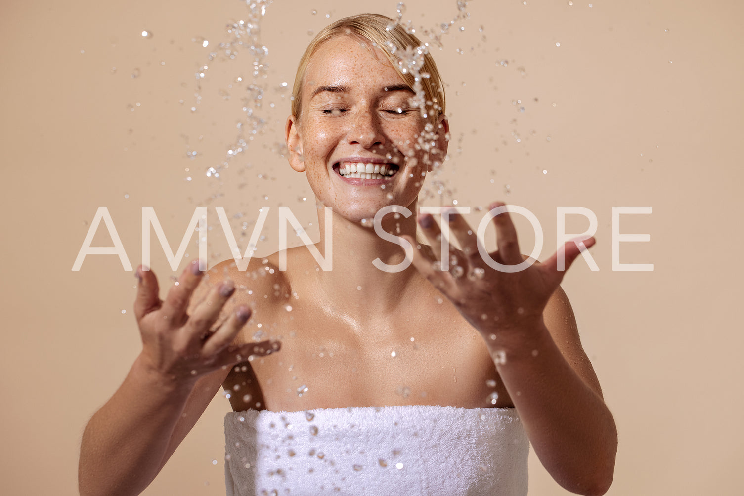 Happy woman wrapped in white towel splashing water on face in st