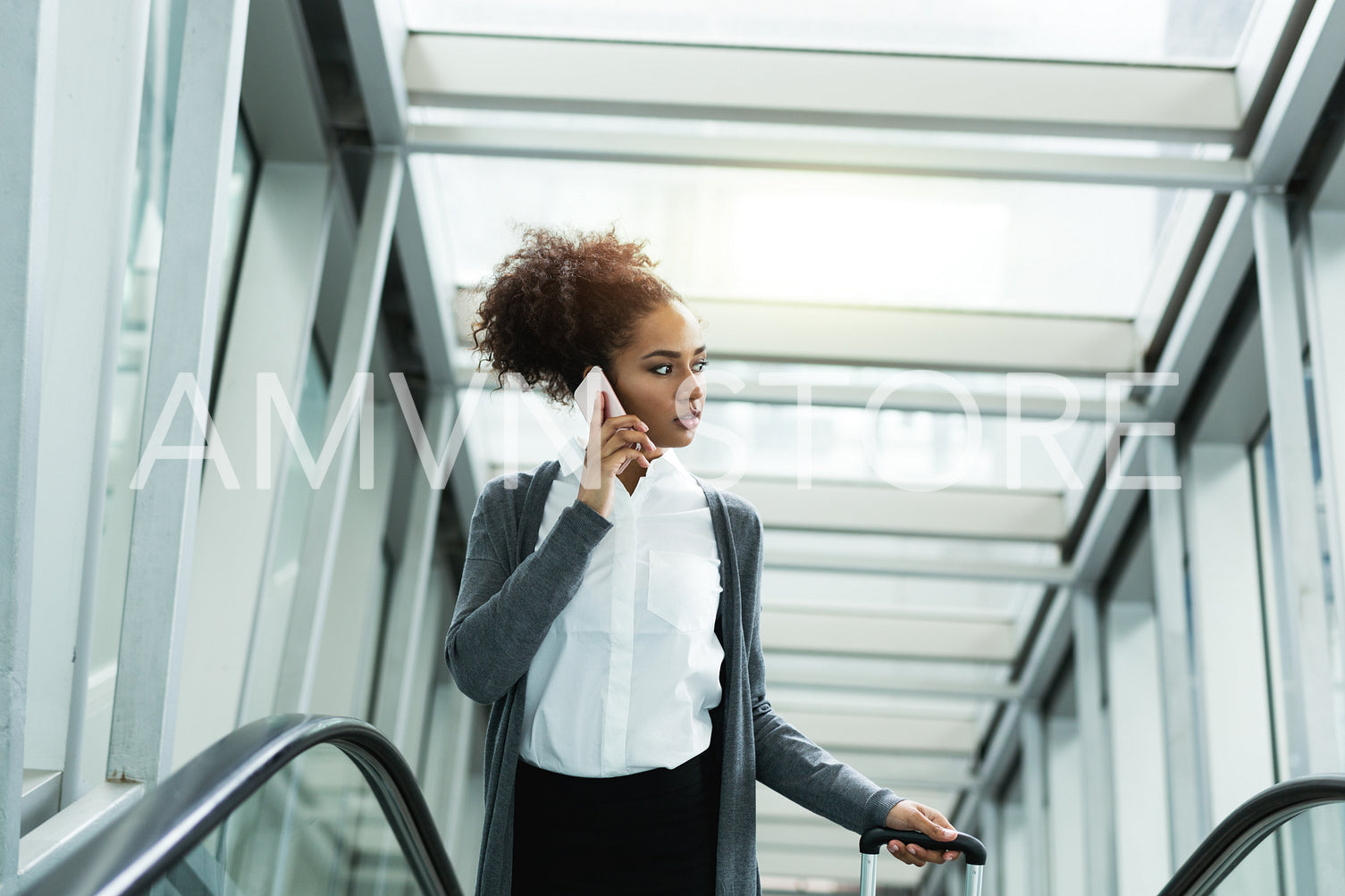 Young woman talking on mobile phone, standing on escalator with suitcase	