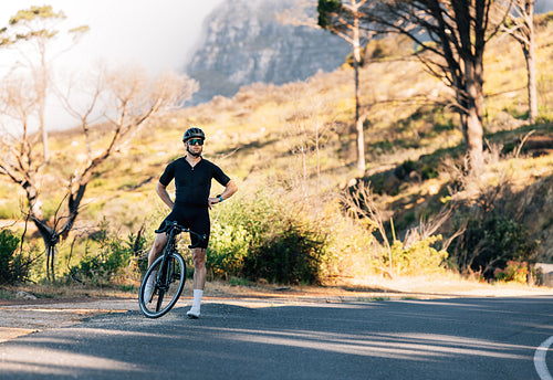 Professional cyclist in black sportswear relaxing on a roadside with hands on a hips