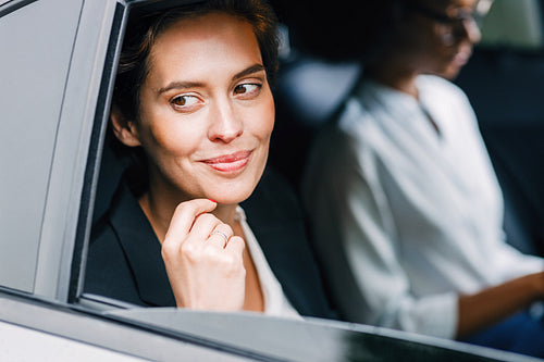 Smiling businesswoman sitting in a cab with her assistant. Two women on a backseat traveling in the car.