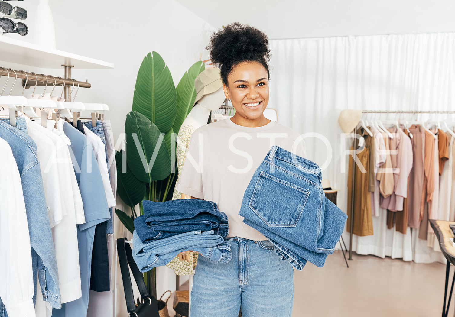 Cheerful saleswoman standing in clothing store with two piles of jeans