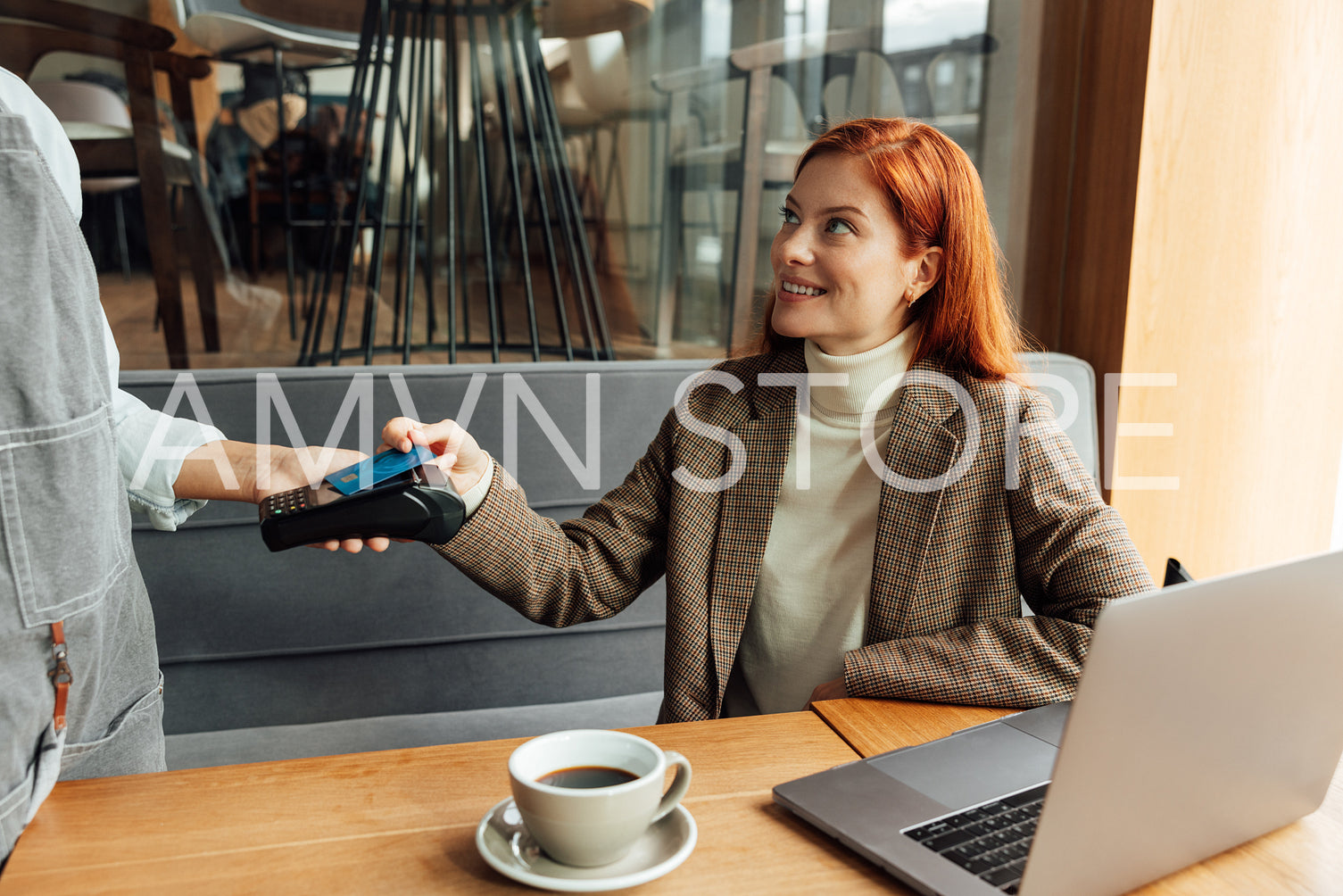 Smiling businesswoman with ginger hair paying by card in coffee shop