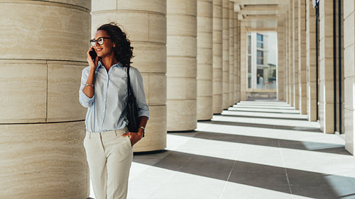 Smiling young african businesswoman walking outdoors and talking on cell phone