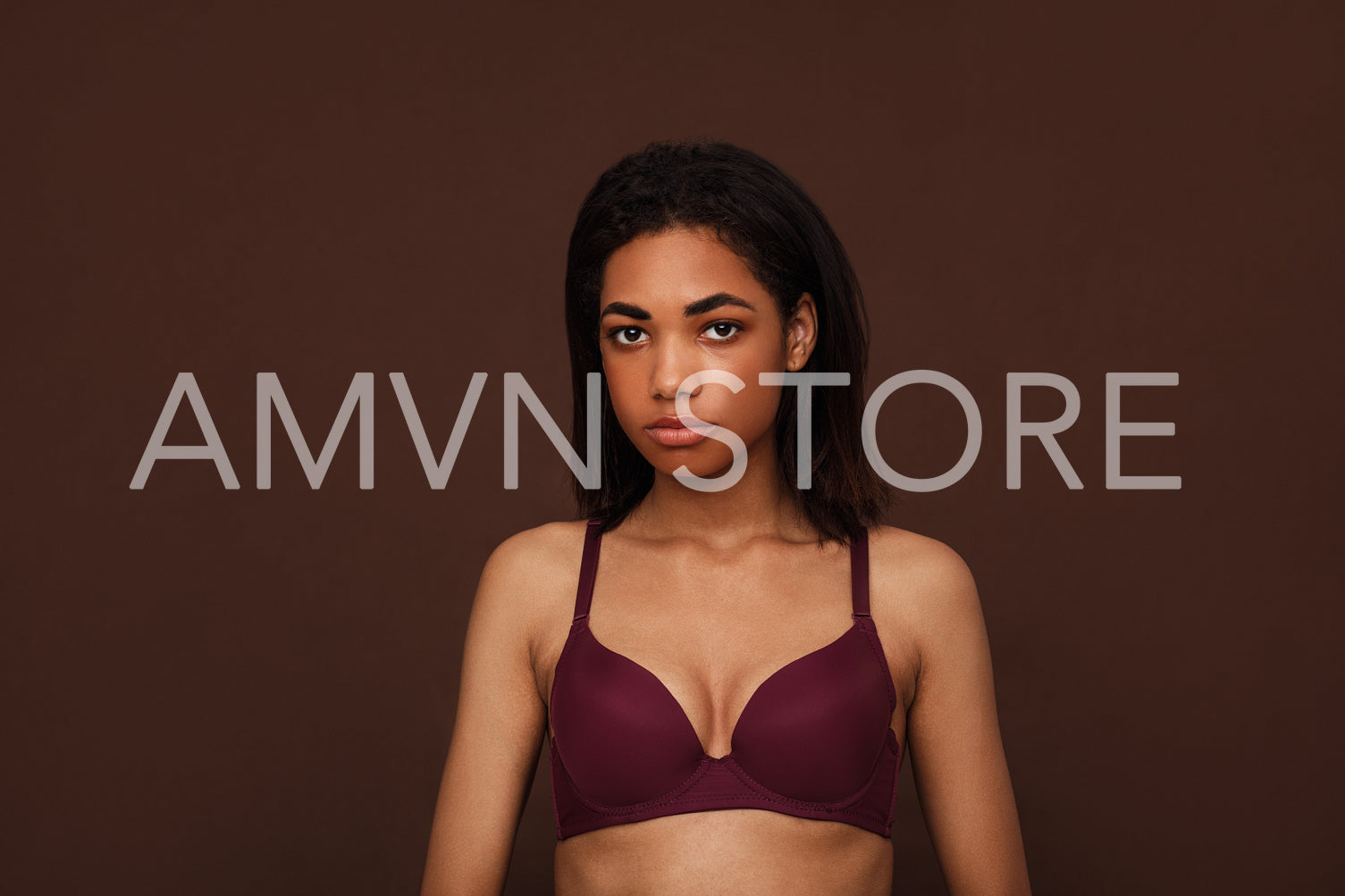 Portrait of a young woman with black hair against brown background. Young slim female in lingerie looking at camera in studio.