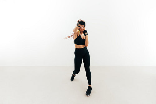 Young woman doing shadow boxing indoors. Muscular female in gloves exercising against a white wall.