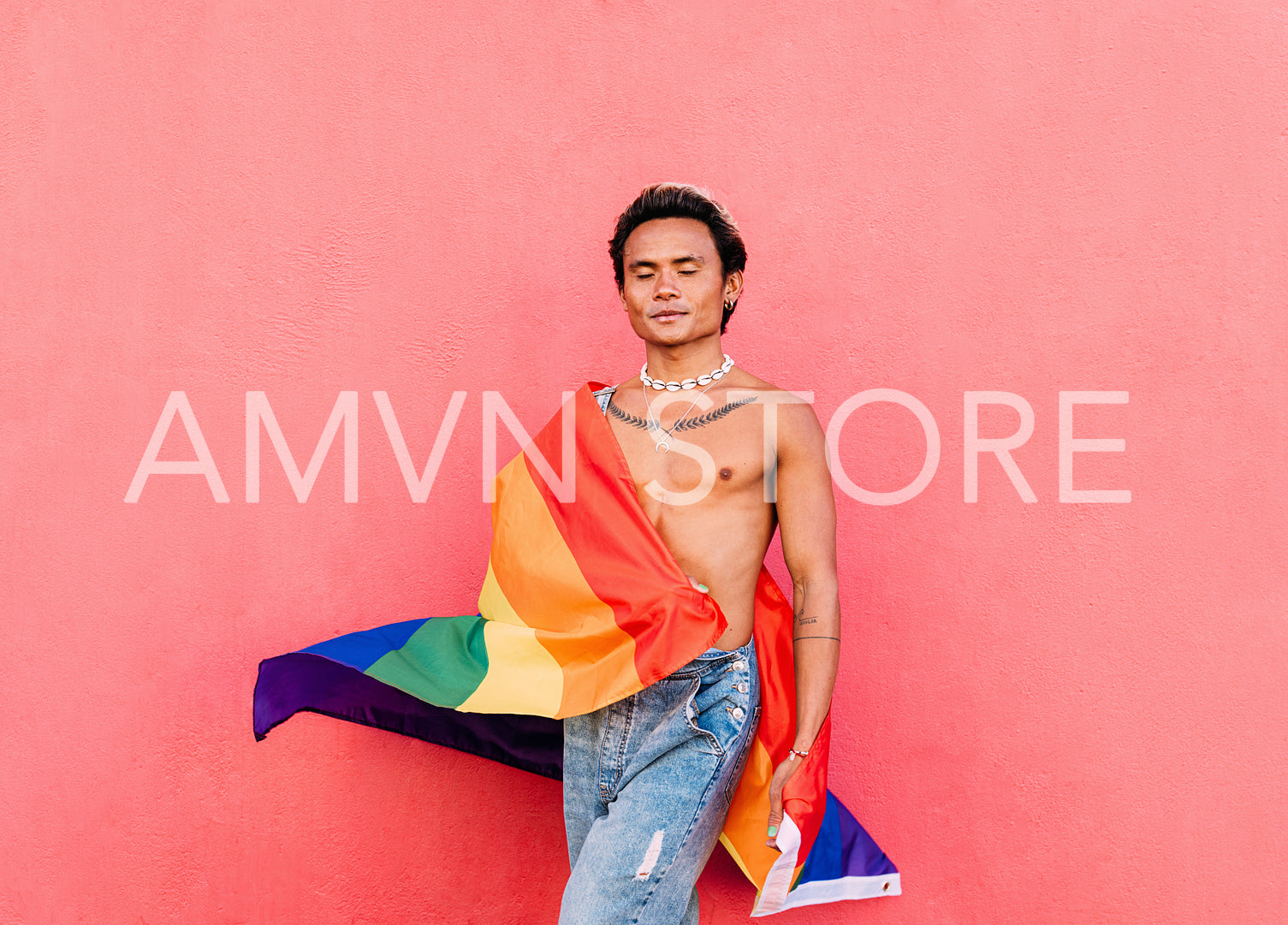 Handsome guy with rainbow lgbt flag standing against pink wall outdoors