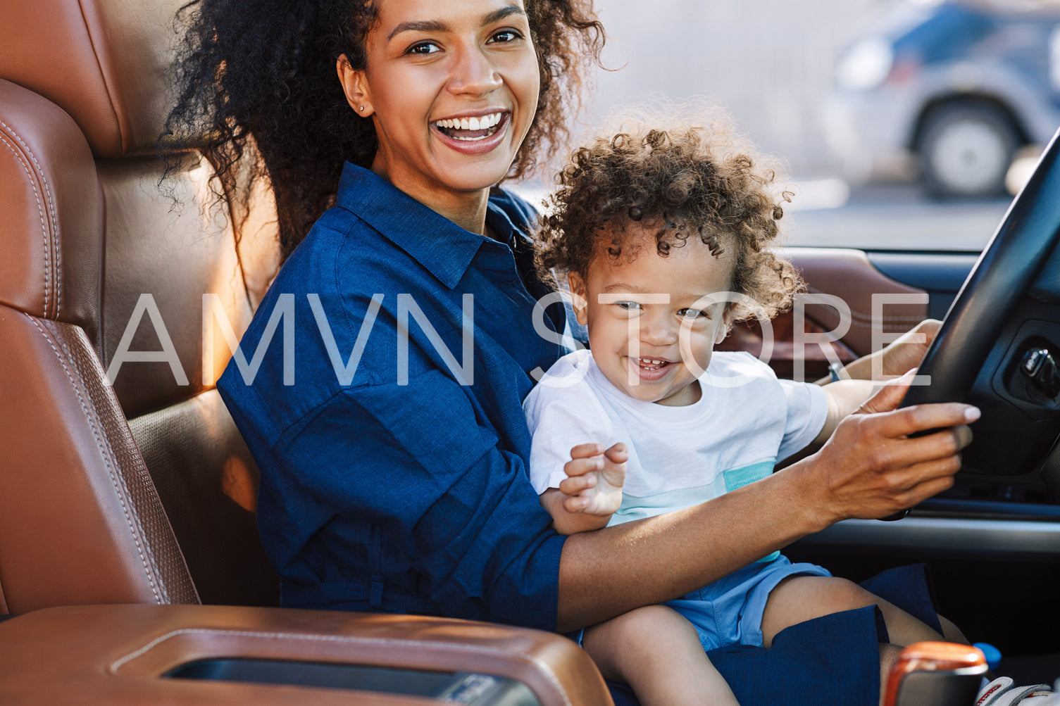 Smiling mother with happy son looking at camera while sitting on car driver seat	