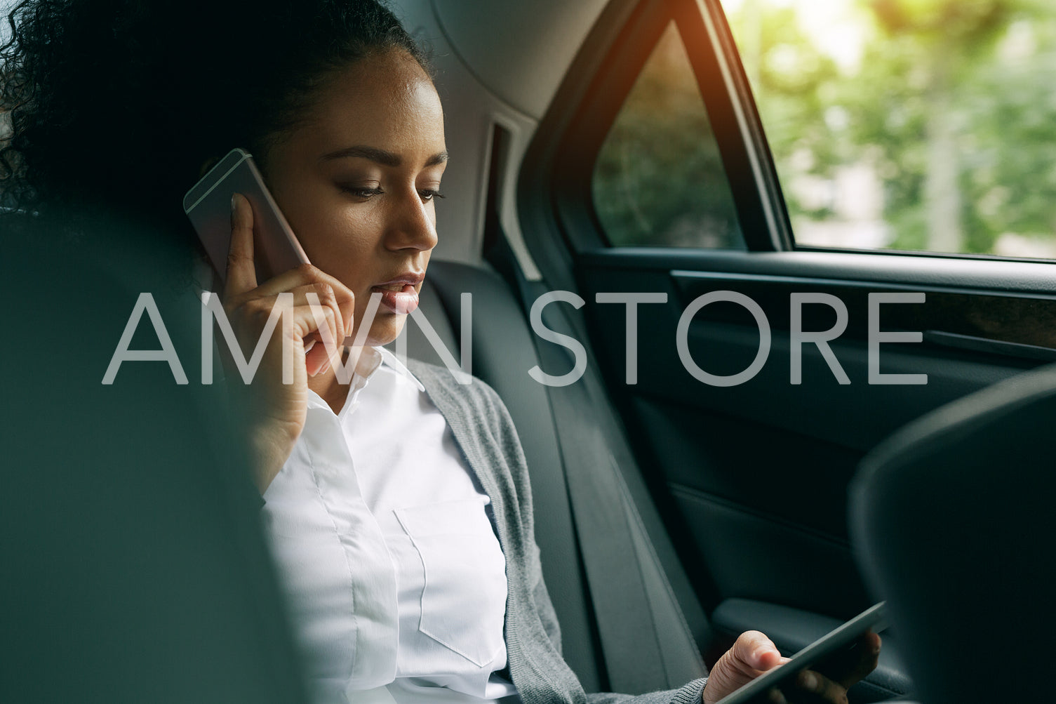 Female entrepreneur looking at digital tablet and talking on mobile phone, sitting on the back seat of a car	