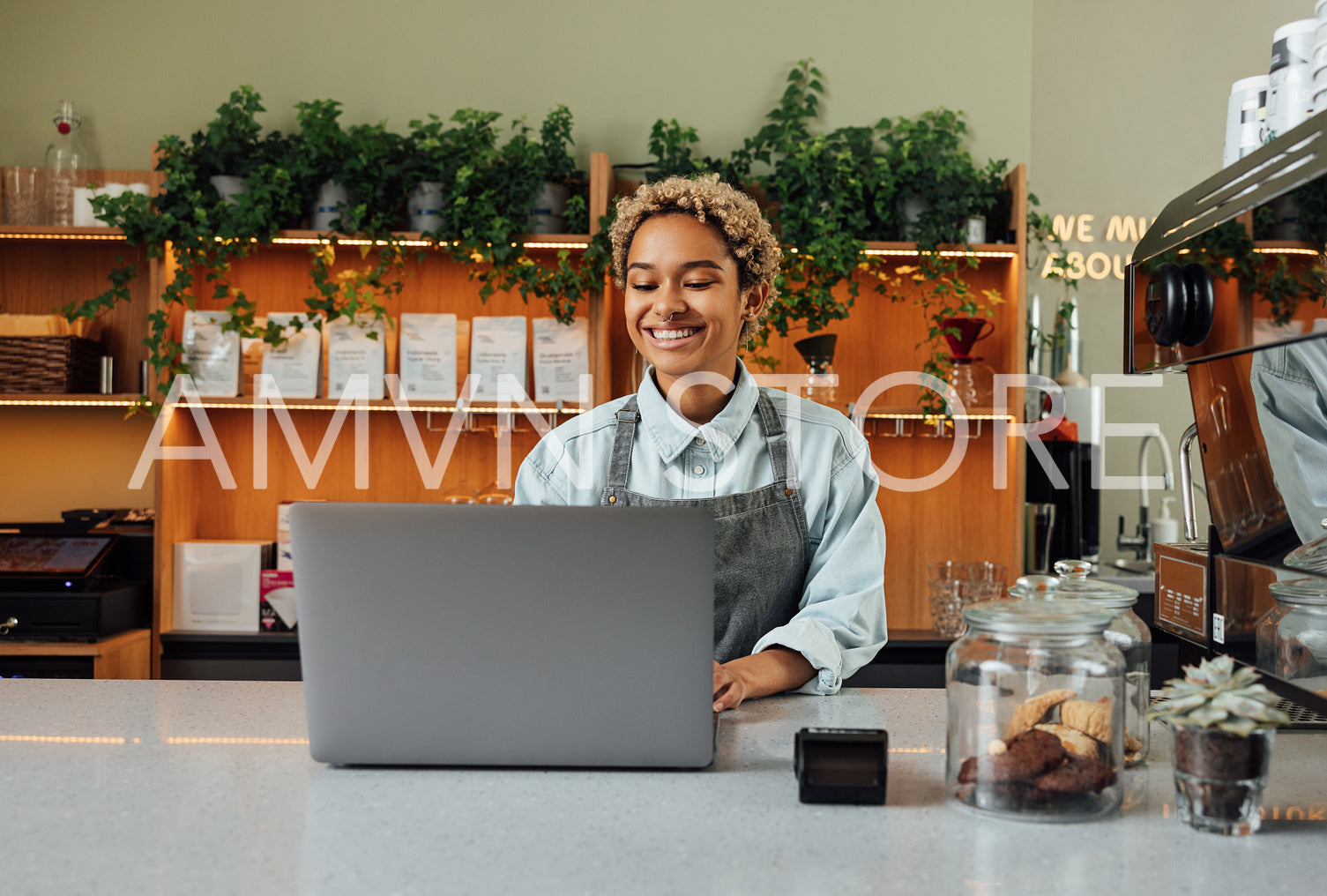 Smiling barista in apron typing on laptop at the counter. Cheerful coffee shop owner working while standing at the bar counter.