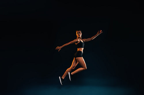 Slim woman working out on black background. Female athlete doing jumps in studio.