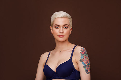 Portrait of a shot haired woman with tattoo on her hand against brown background