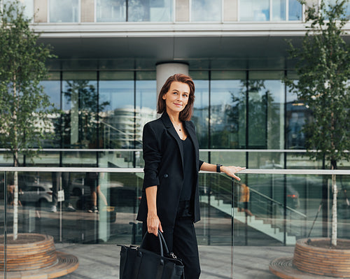 Side view of a confident middle-aged businesswoman with a bag standing against an office building