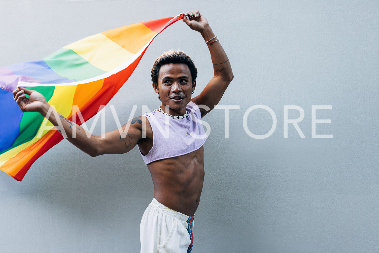 Young man holding rainbow flag at grey wall