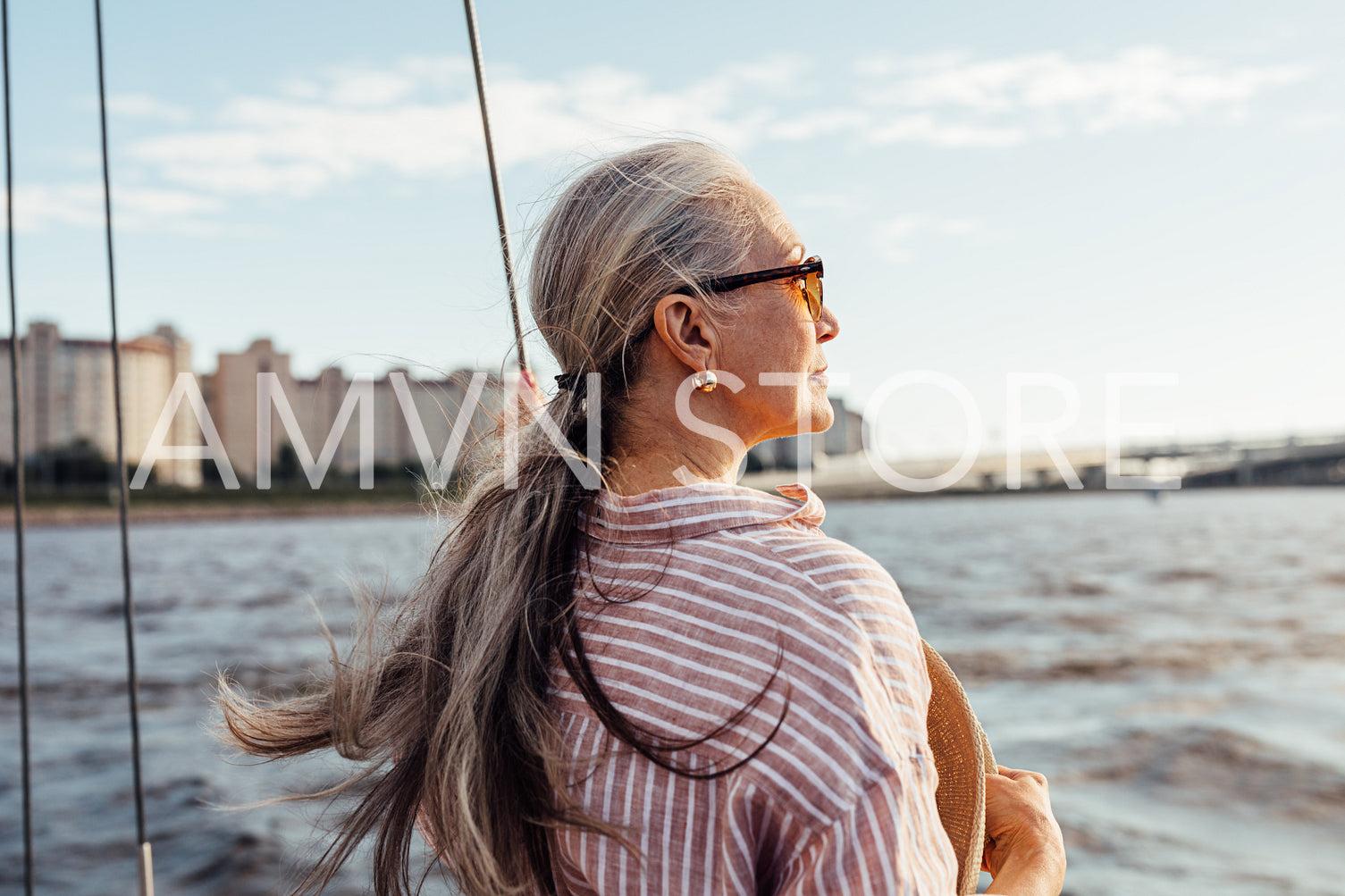 Side view of mature woman wearing sunglasses and looking to the distance while standing on the yacht	