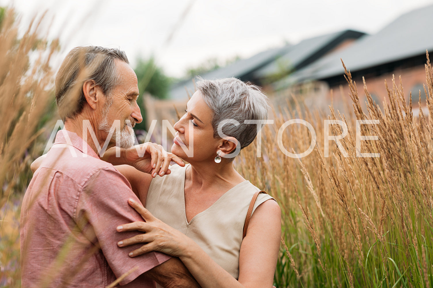 Two aged people standing together in the field. Senior wife and husband are looking at each other and embracing the outdoors.